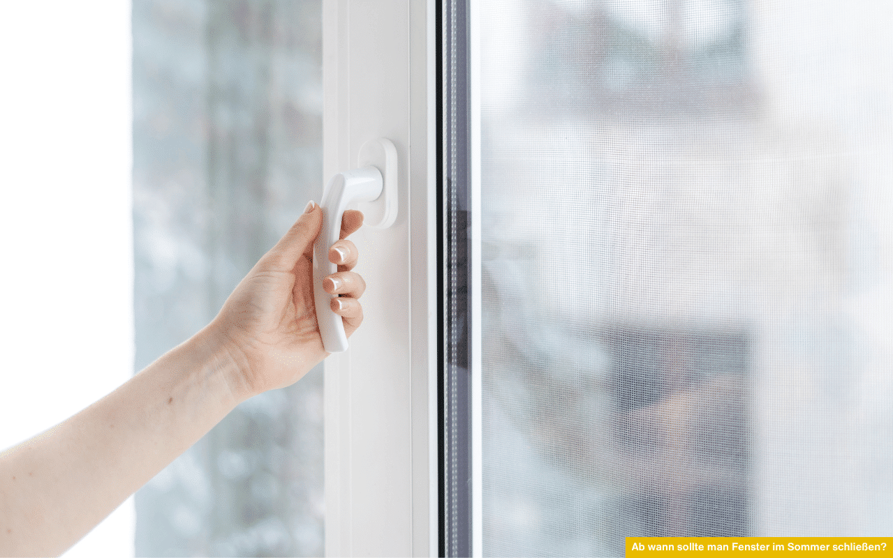 Ab wann sollte man Fenster im Sommer schließen zeigt eine Hand, die ein weißes Kunststofffenster vor einem Insektenschutzgitter schließt.