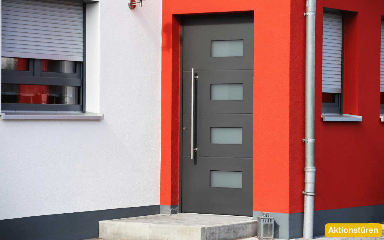 Aktionstüren – moderne graue Haustür mit vier Glaseinsätzen an einer rot-weißen Hausfassade