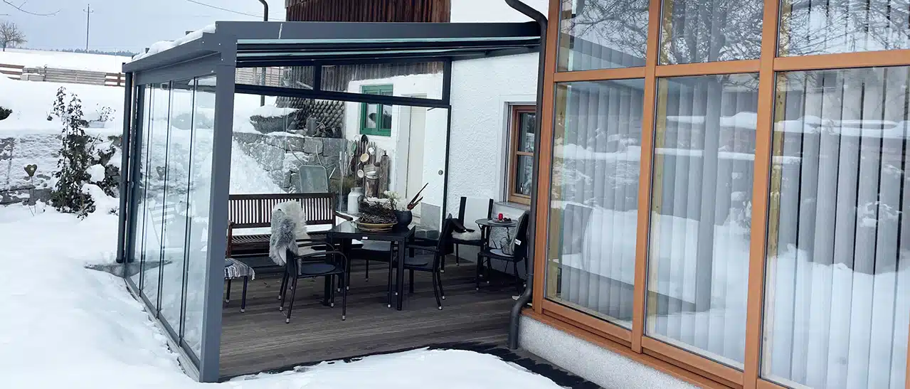 Moderne graue Aluminium-Terrassenüberdachung als Wintergarten-Alternative, mit geschlossenen Seitenwänden, schützt vor Wind und Regen.