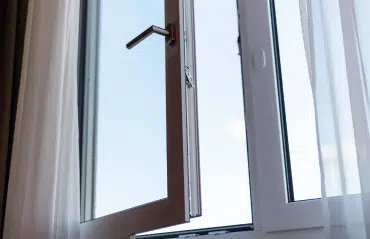 Nahaufnahme eines leicht geöffneten weißen Kunststofffensters mit Blick auf den Griff und die Scharniermechanik.