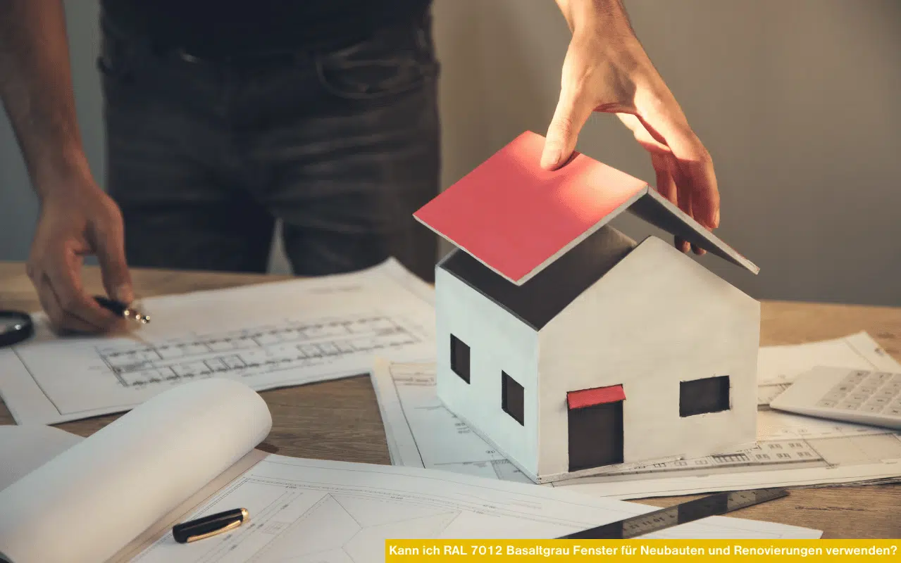Architekt mit Hausmodell und Bauplänen zeigt das Thema „Kann ich RAL 7012 Basaltgrau Fenster für Neubauten und Renovierungen verwenden?“