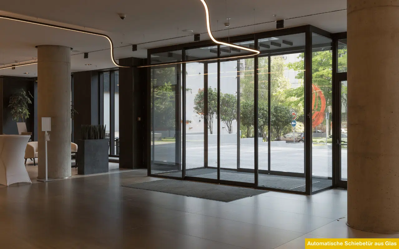 Automatische Schiebetür aus Glas im modernen Eingangsbereich eines Gebäudes mit Glasfassade und Beleuchtung