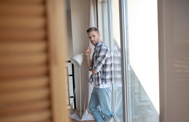 Balkontürgrößen - Junger Mann lehnt sich an individuell angepassten, großflächigen Balkontüren an, symbolisiert kundenorientierte Maßanfertigung für Türen.