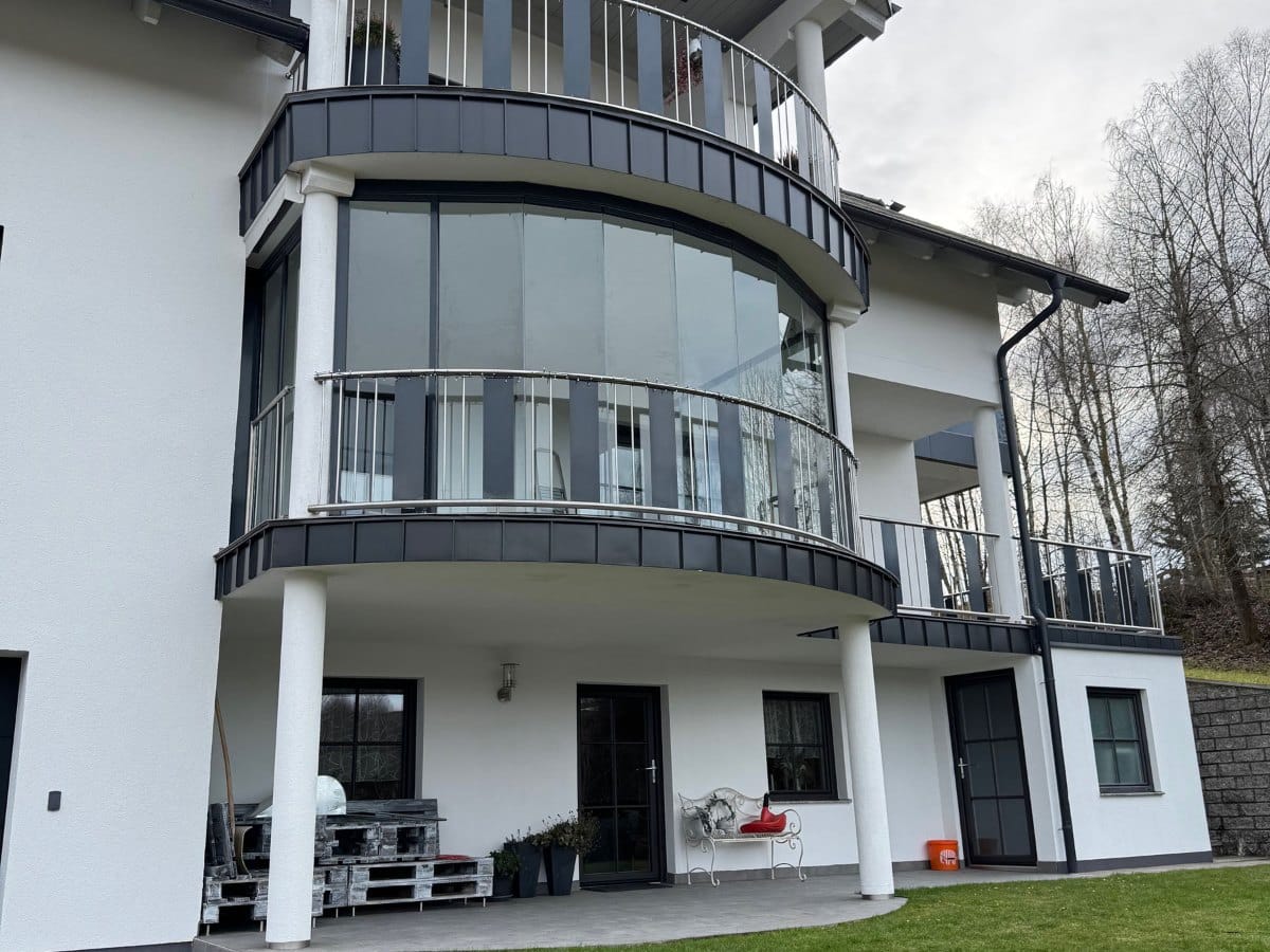 Nachträglich verglaster runder Balkon mit Schiebe-Dreh-System an einem weißen Wohnhaus