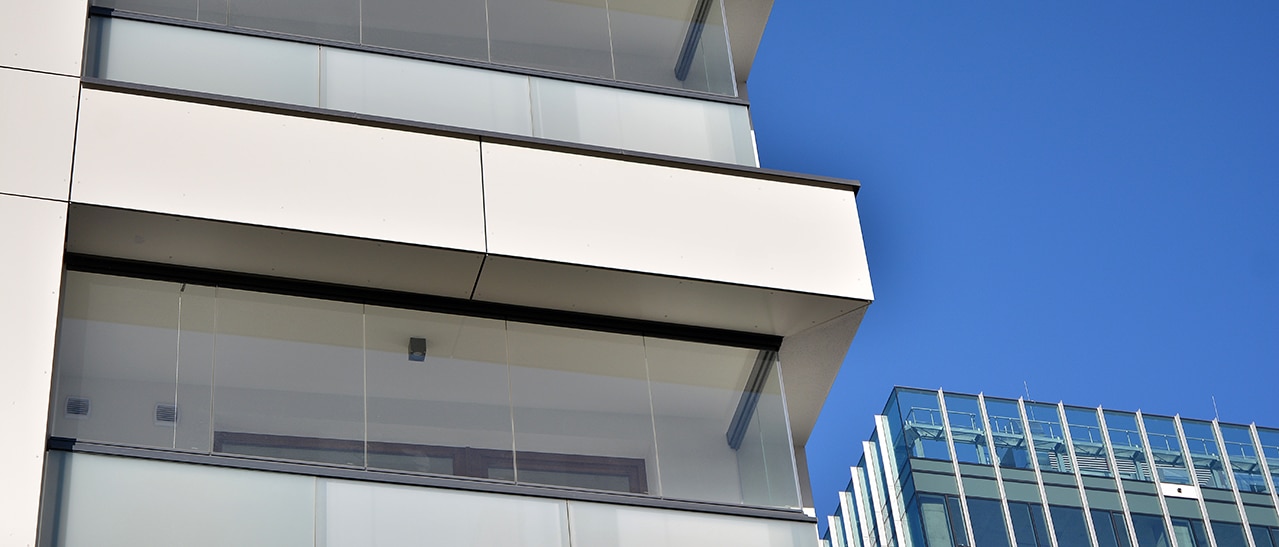 Moderne Balkonverglasung als Lärmschutz. Die Außenansicht verdeutlicht, wie transparente Glassysteme die Architektur ergänzen und gleichzeitig eine effektive Schallschutzbarriere für die Bewohner schaffen, ohne den Lichteinfall zu mindern.