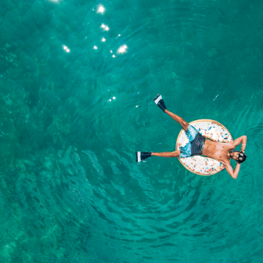 Betriebsurlaub von 3. bis 14. August 2026 Mann treibt entspannt auf türkisem Wasser