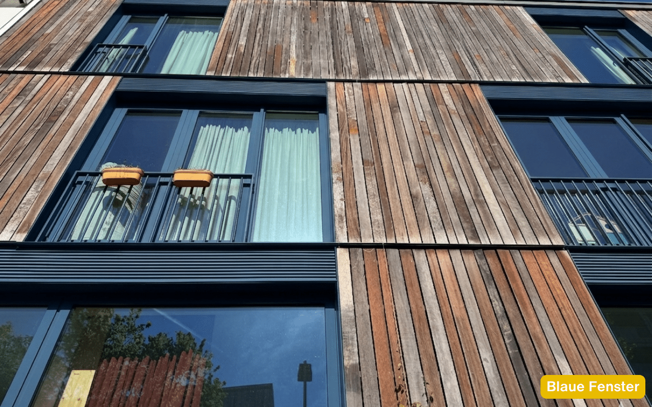 Blaue Fenster an moderner Wohnhausfassade mit vertikaler Holzlattenverkleidung in verschiedenen Brauntönen