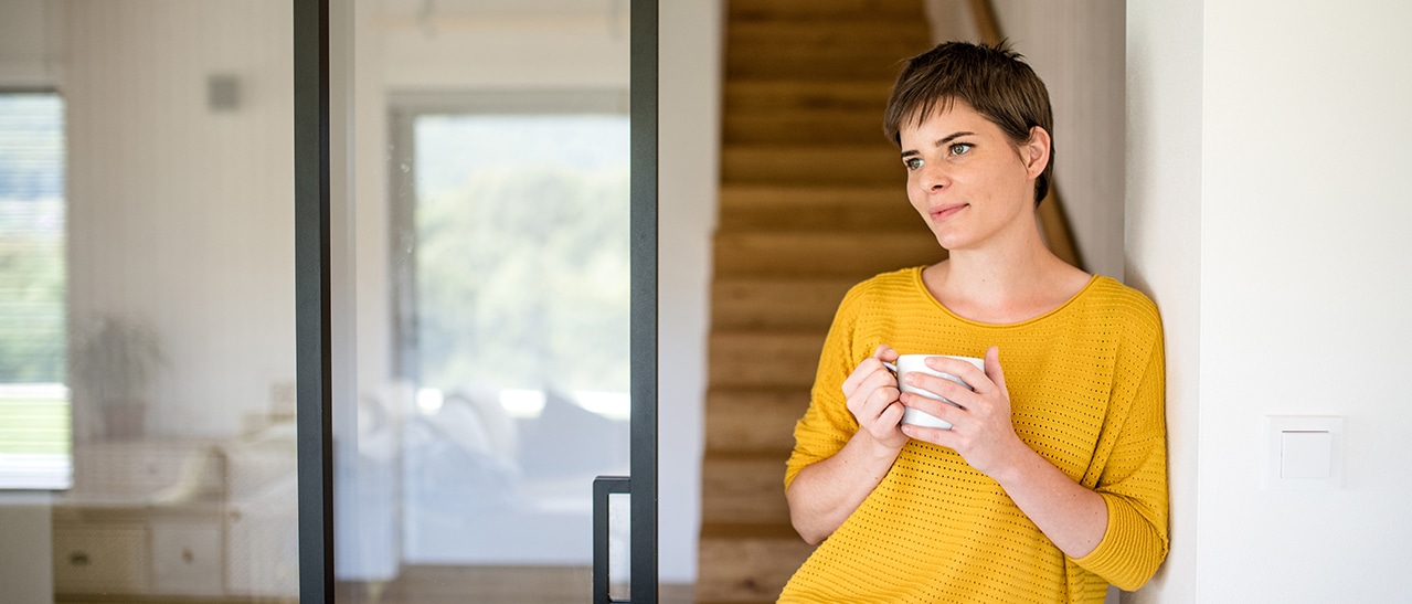 Im Vordergrund steht eine Frau mit Kaffeetasse, im Hintergrund eine große, elegante Glastür – modernes Fensterdesign im Innenraum.