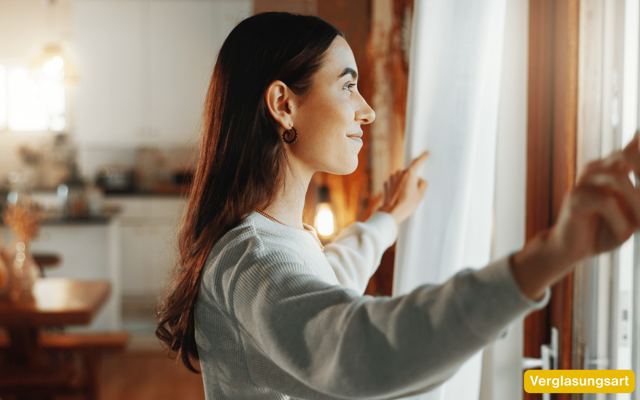 Die passende Verglasungart für Energieeffizienz zeigt eine junge Frau, die lächelnd aus dem Fenster blickt.