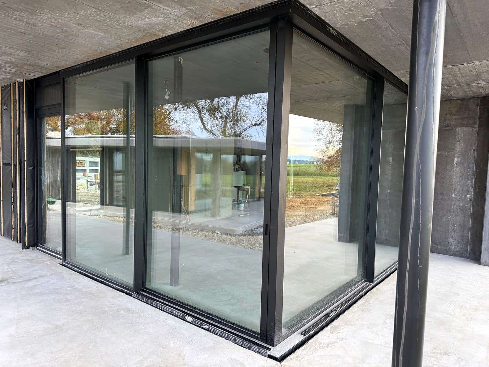 Eckverglasung mit wärmegedämmten Aluminium-Schiebefenstern an einem Sichtbeton-Neubau im Rohbau, Außenansicht unter dem Vordach, Oberösterreich