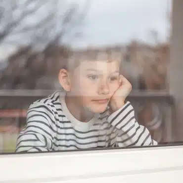 Ein Junge sitzt hinter einem Fenster und fragt sich, warum Fenster knacken und Geräusche machen.