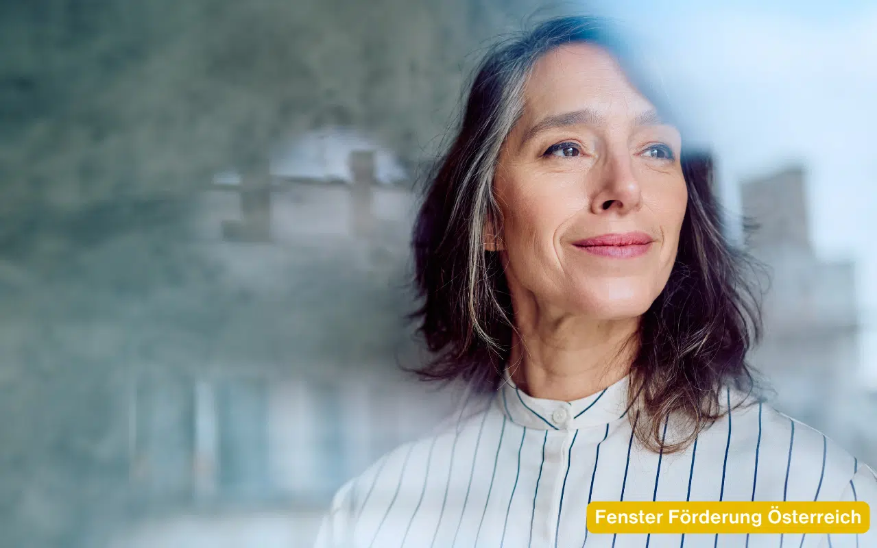 Eine Frau hinter einem sauberen Fenster. Fenster Förderung Österreich für den Tausch alter Scheiben.