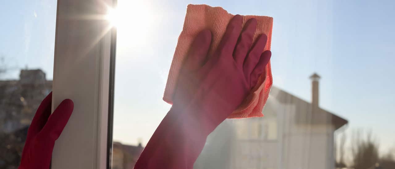 Eine Frau trocknet nach dem Fensterputzen im Winter sorgfältig die Fensterscheibe mit einem Tuch ab.