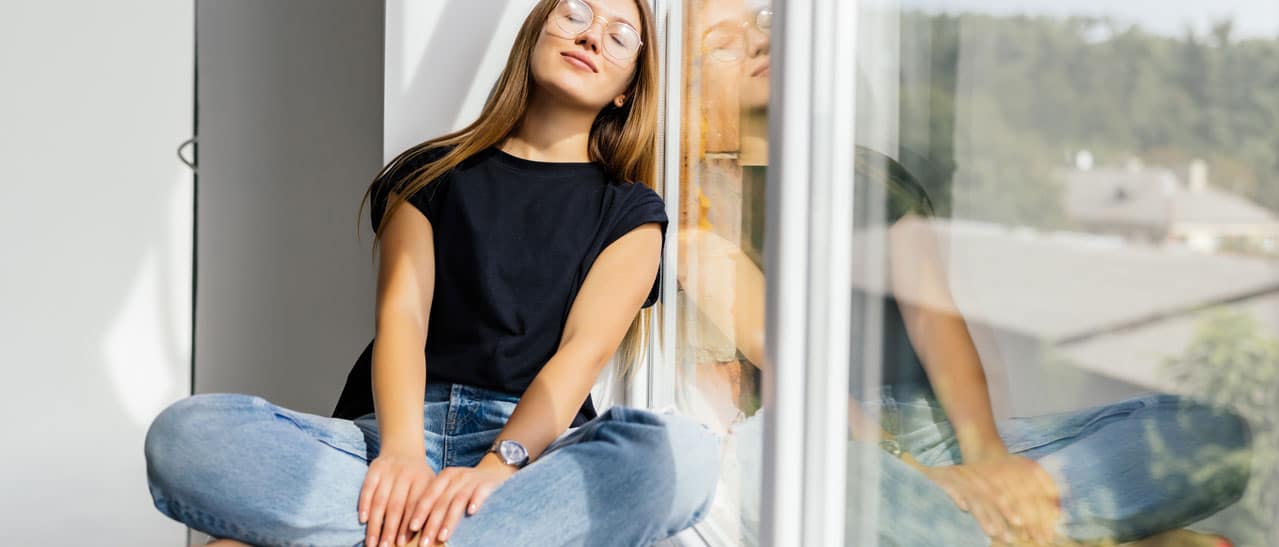 Eine junge Frau in Steyr genießt die neuen Fenster von Fenster-Schmidinger, die Wärme im Winter und Schutz vor Sommerhitze bieten.