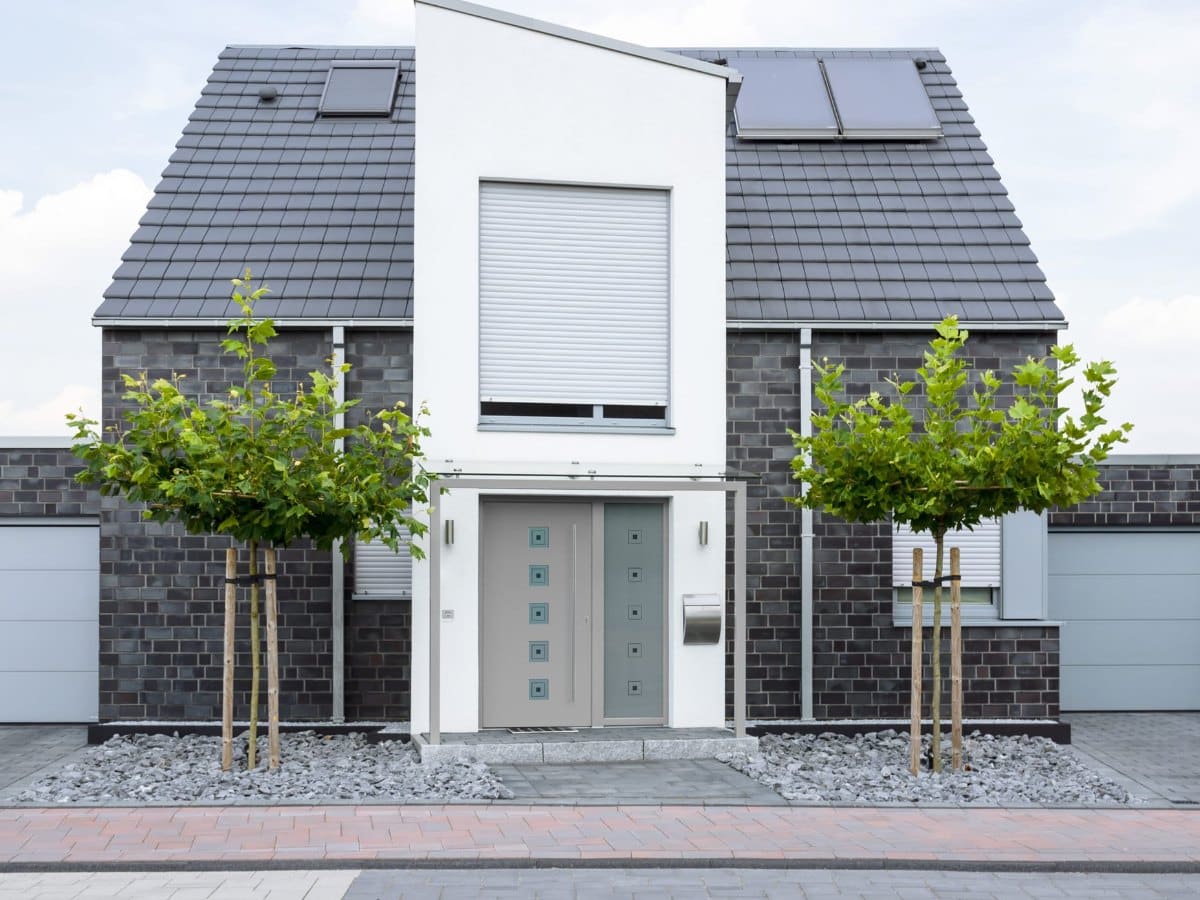 Graue Aluminium-Eingangstür mit fünf quadratischen sandgestrahlten Glasfeldern und fixem Seitenteil an einem Einfamilienhaus