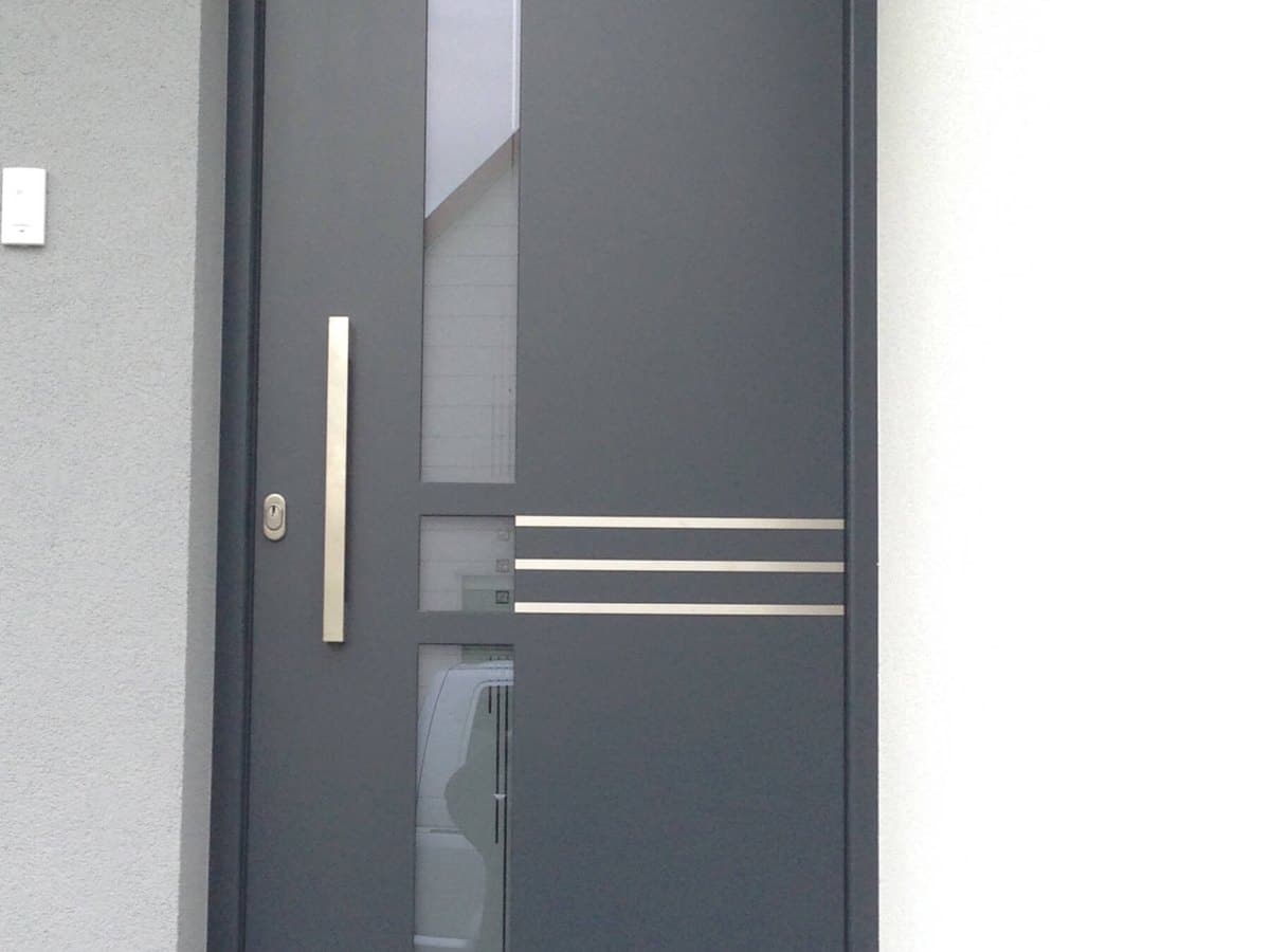 Flächenbündige Aluminium-Eingangstür in Anthrazit mit Edelstahllisenen und Stangengriff an einem Einfamilienhaus in Oberösterreich