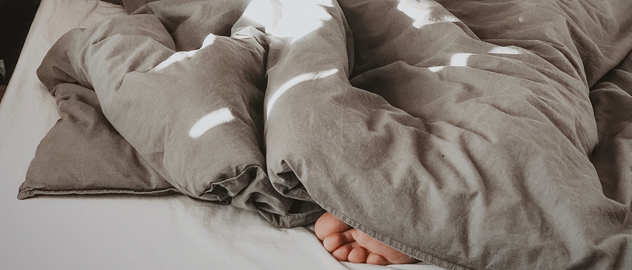 Person liegt gemütlich im Bett, erholt dank Schallschutzfenster RAL 8019 Graubraun. Diese Fenster schaffen eine ruhige Schlafoase.