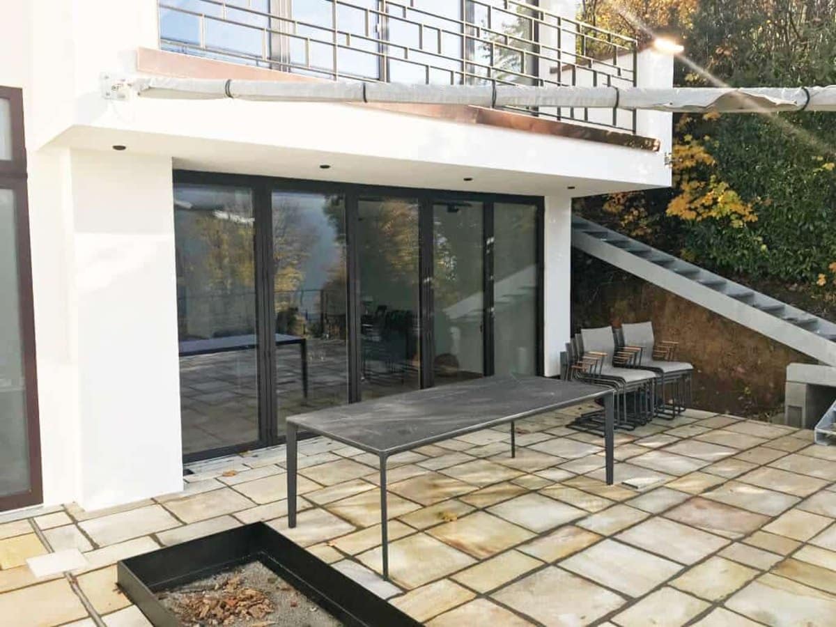 Faltschiebetür zur Terrasse, außen in RAL 8019 Graubraun, an einem weißen Haus mit Steinplatten-Terrasse