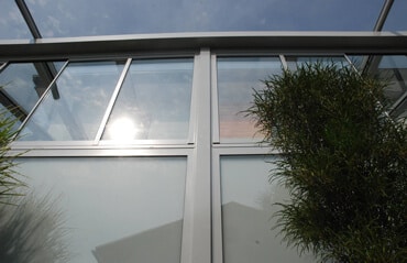 Modernes Wohnhaus mit einem Wintergarten-Anbau und integrierten Glas-Faltwänden für einen nahtlosen Übergang in den Garten.