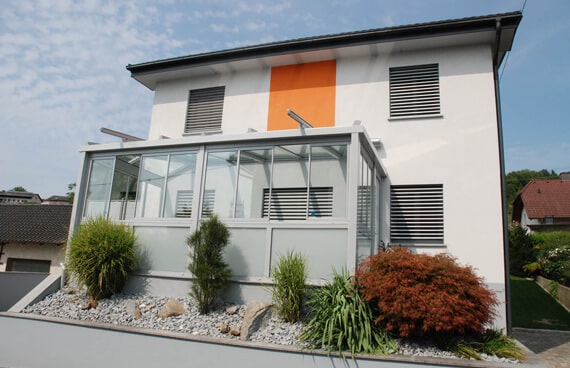 Modernes Wohnhaus mit einem Wintergarten-Anbau und integrierten Glas-Faltwänden für einen nahtlosen Übergang in den Garten.