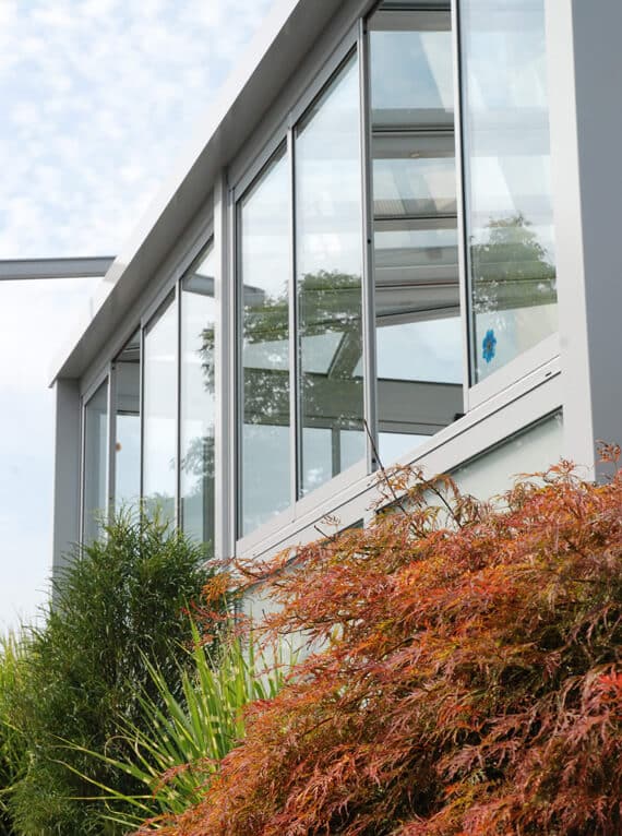Referenzprojekt einer modernen Glas-Faltwand mit hellgrauem Rahmen und harmonischer Gartenbepflanzung.