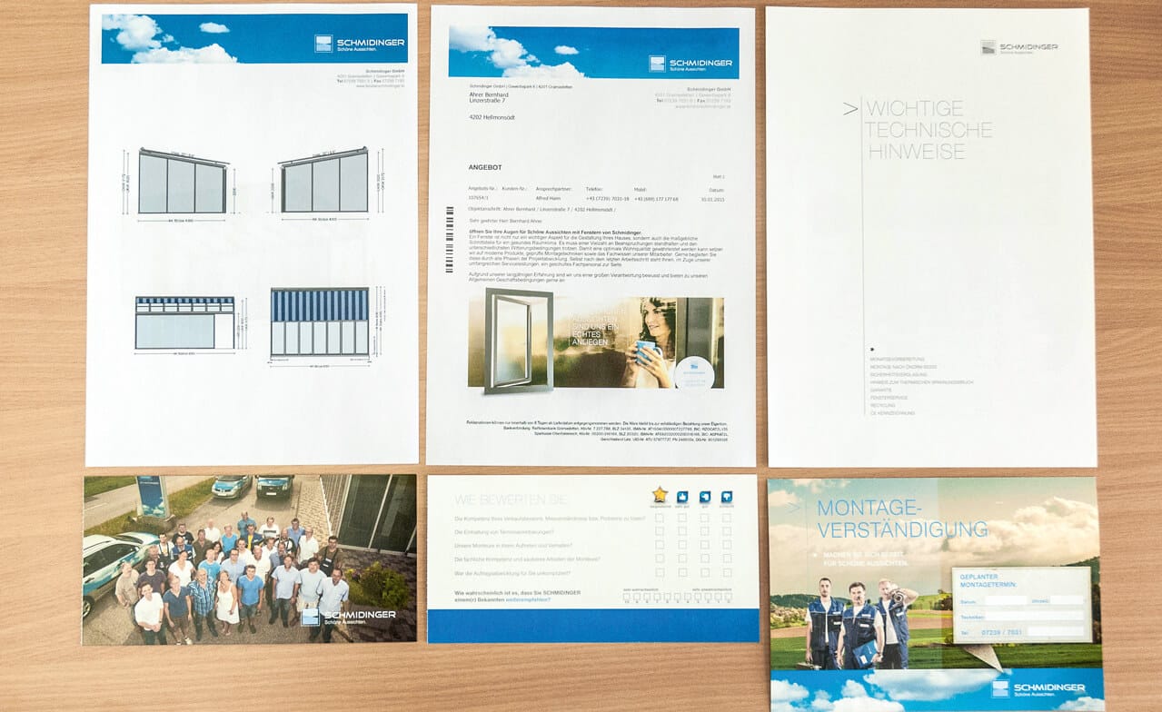 Foto von Prospekten und Angebotsdokumenten, ordentlich aufgelegt. Oben sind technische Zeichnungen zu sehen, unten Gruppenfoto und Markenunterlagen – wirkt wie ein komplettes Angebots-Set.