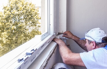 Fenstermonteur dichtet Fensterbankbereich mit Abdichtungsfolie während des Fenstertauschs ab.