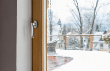 Fenster in Freistadt mit Holzrahmen und Griff, Blick von innen auf verschneite Terrasse und winterliche Umgebung