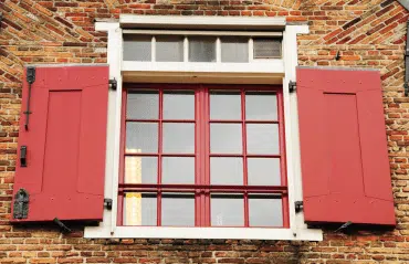 Fenster in RAL 3000 Feuerrot mit klassischen Klappläden an historischer Ziegelfassade