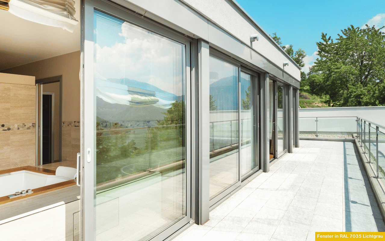 Zu sehen ist eine elegante, durchgehende Fensterfront aus Aluminium in Lichtgrau. Die klaren Linien und großen Glasflächen sorgen für helle Innenräume und verbinden Wohnraum und Terrasse optisch miteinander.