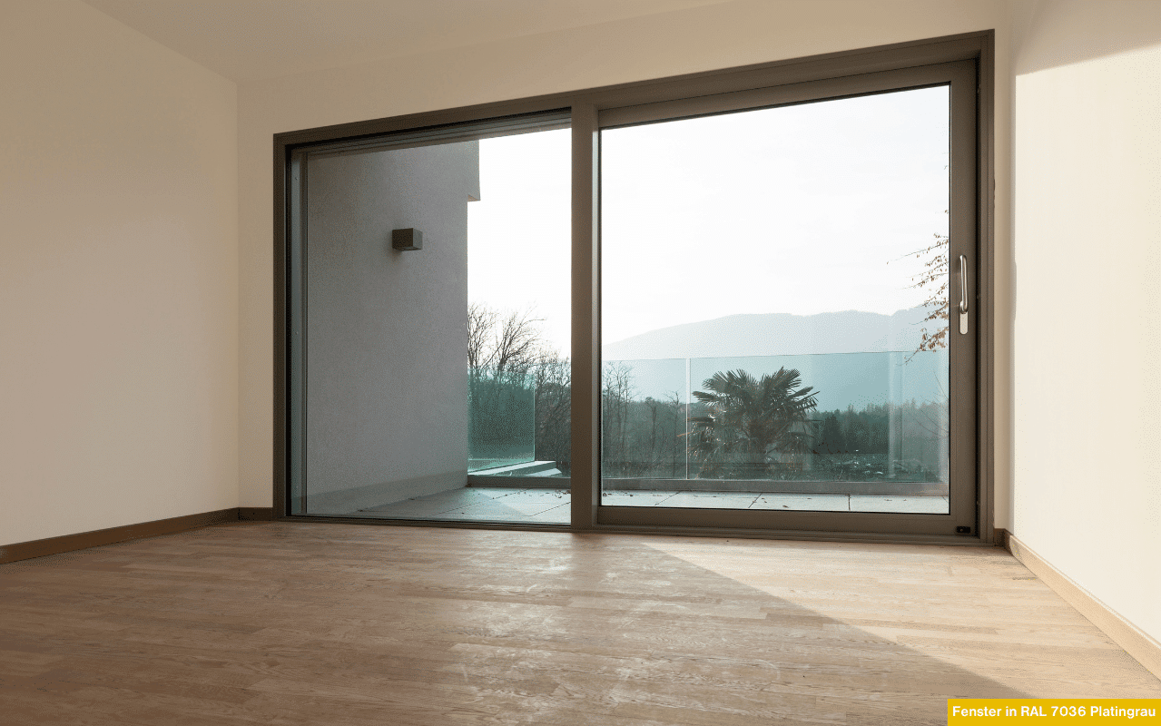 Ein modernes Schiebefenster in Platingrau öffnet den Raum nach außen. Das Glas reflektiert das natürliche Licht, während der dezente Farbton ein harmonisches, zeitloses Wohnambiente schafft.