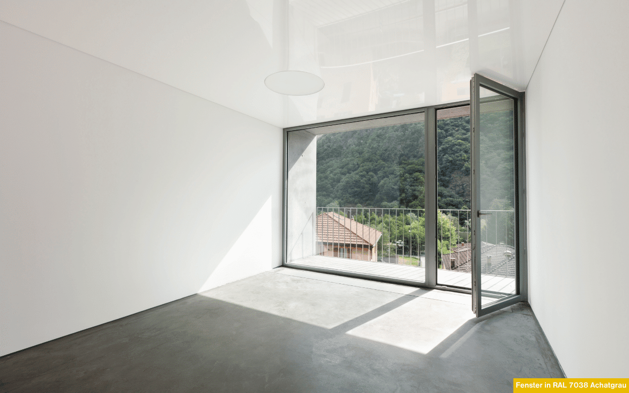 Ein modernes, geöffnetes Fenster mit schlanken Aluminiumprofilen in Achatgrau bietet freien Blick auf eine grüne Hügellandschaft. Die klare Gestaltung schafft Helligkeit, Transparenz und eine ruhige Atmosphäre im Innenraum.