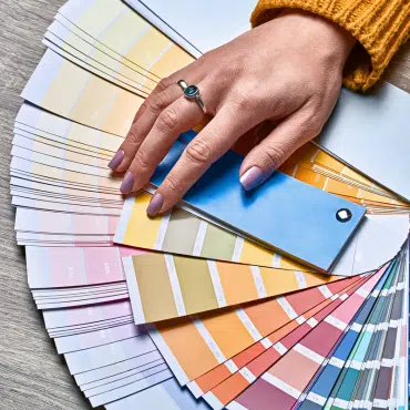 Eine Frau hält ihre Hand über einen Farbfächer zur Auswahl neuer Fenster. Besonders beliebt ist Fenster in RAL 7040 Fenstergrau.