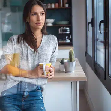 Fenster in RAL 8017 schokoladenbraun bringt Gemütlichkeit in die Küche während eine Frau entspannt ihren Kaffee genießt.