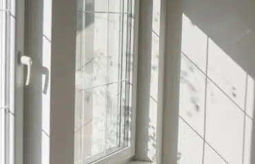 Fenster in RAL 9016 Verkehrsweiß in heller Zimmerecke mit Sprossen und Sonnenlicht
