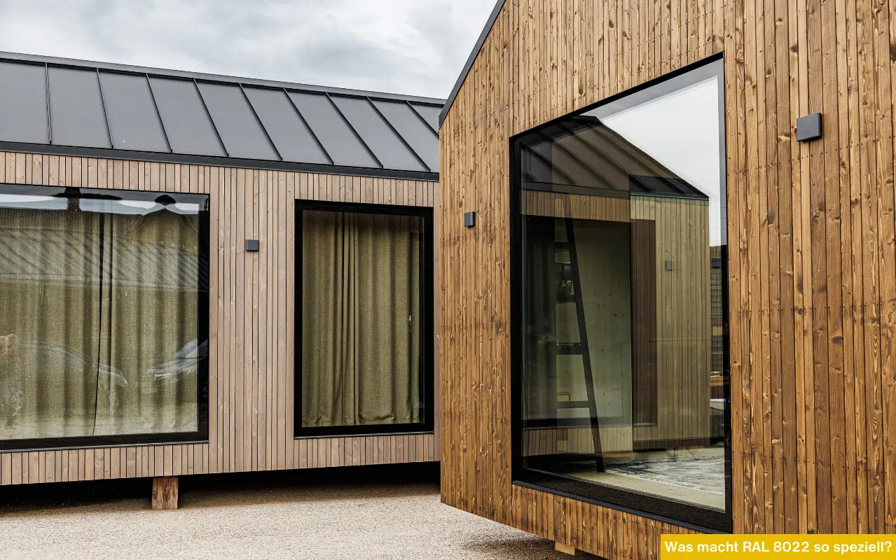 Moderne Holzhäuser mit großen Fenstern in RAL 8022 Schwarzbraun und dunklem Metalldach bei bewölktem Himmel.