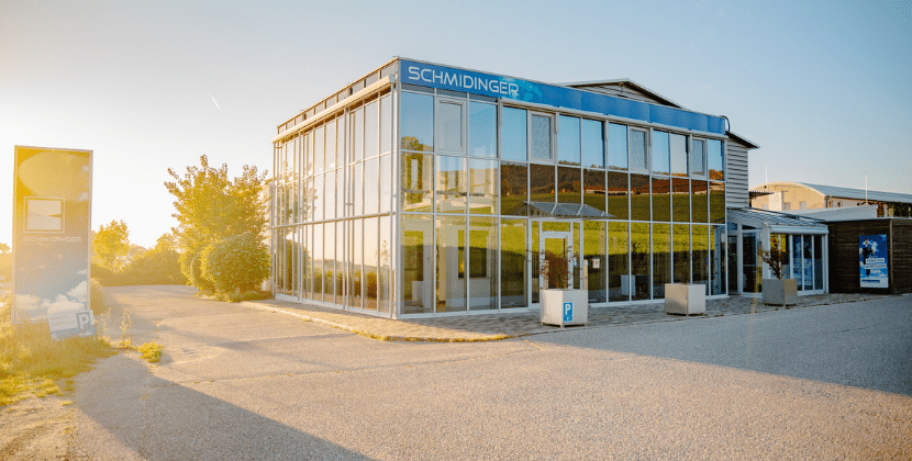 Das moderne Firmengebäude der Schmidinger GmbH mit großer Glasfassade und Schauraum bei Sonnenuntergang.