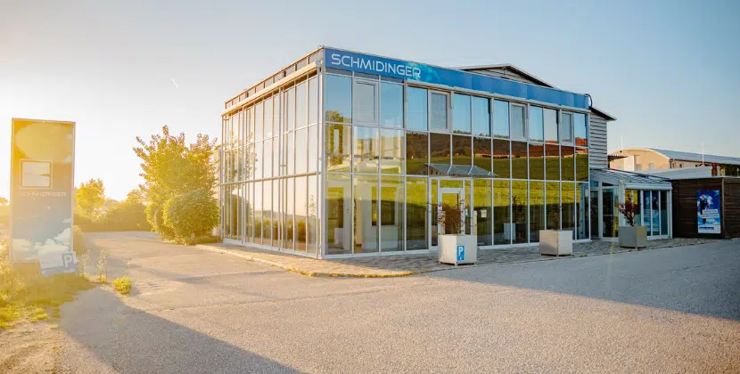 Das moderne Firmengebäude der Schmidinger GmbH mit großer Glasfassade und Schauraum bei Sonnenuntergang.