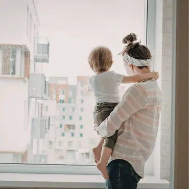 Fenster Vöcklabruck – Mutter und Kind am hellen Fenster mit Aussicht auf moderne Architektur für lichtdurchflutetes Wohnen