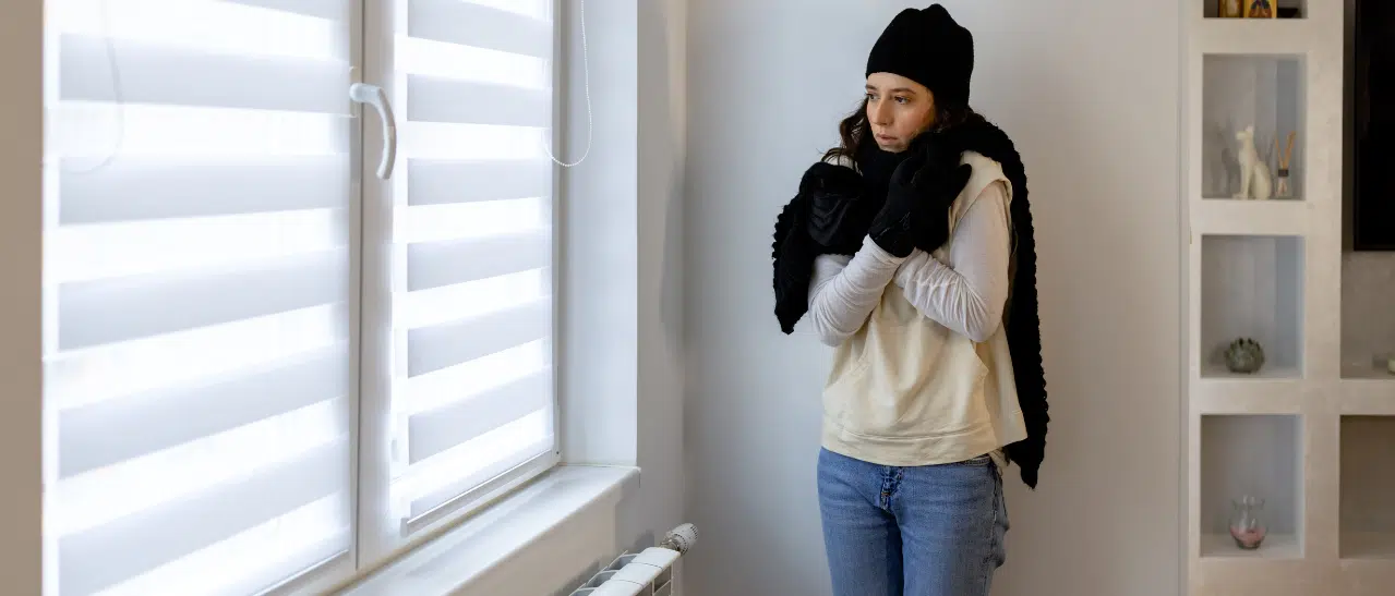 Eine Frau in der Wohnung mit Schal und Haube, da es trotz moderner Fenster kalt ist. Fensterservice Oberösterreich hilft bei undichten Fenstern.