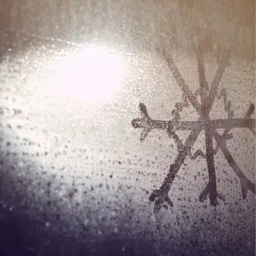 Detailansicht einer Schneeflocke aus Eiskristallen am Fensterglas. Hinweis auf den jährlichen Fenstercheck im Frühling nach der Kälteperiode.