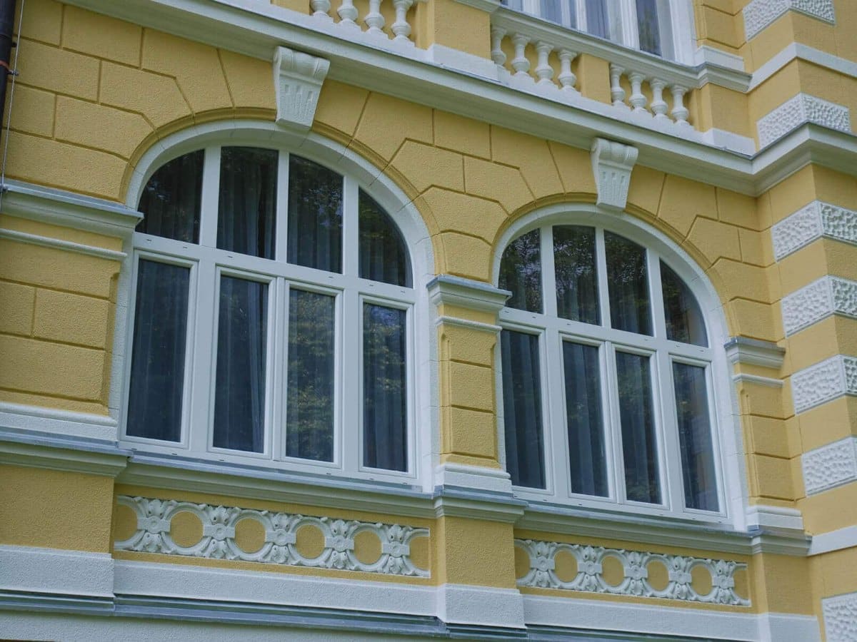 Weiße Rundbogenfenster in einer gelben Altbaufassade mit Stuckverzierungen