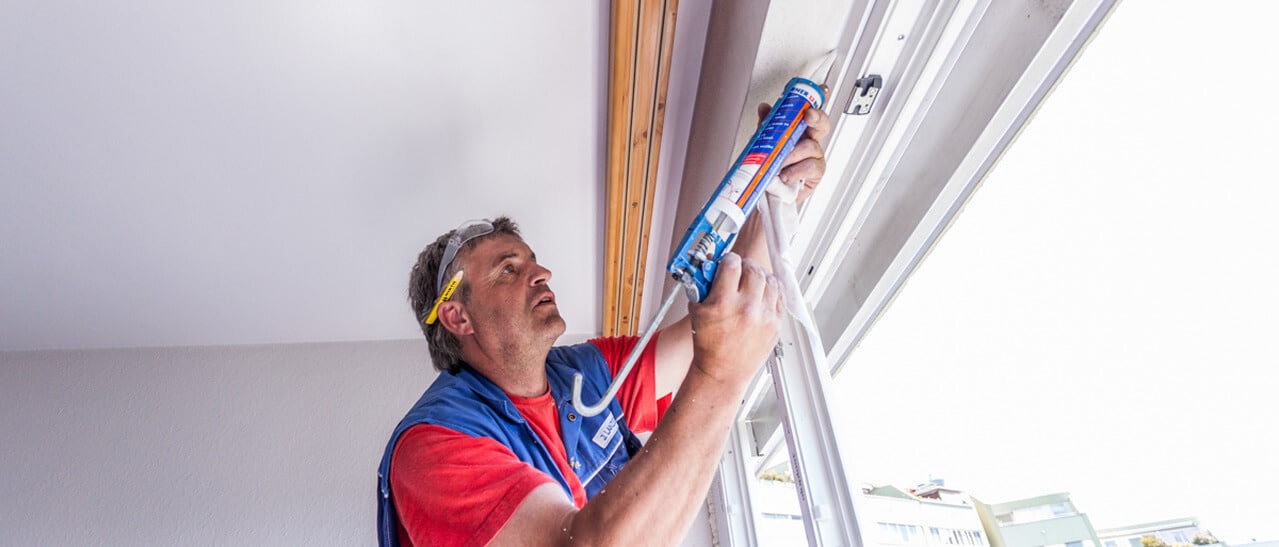 Handwerker bei der präzisen Abdichtung eines Fensterrahmens mit einer Kartuschenpresse während eines Fenstertauschs.