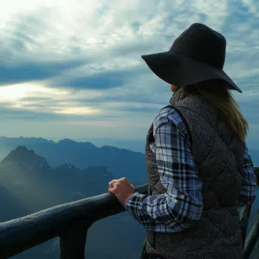 Fenstertrends 2024 - Frau schaut hoffnungsvoll vom Berggipfel in die Ferne, umgeben von atemberaubender Naturkulisse.
