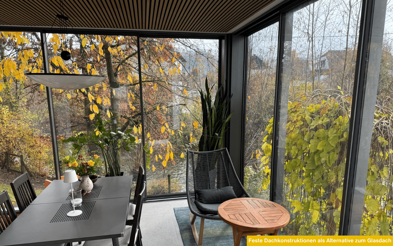 Feste Dachkonstruktionen als Alternative zum Glasdach im gemütlichen Wintergarten mit großflächigen Verglasungen und herbstlichem Ausblick.