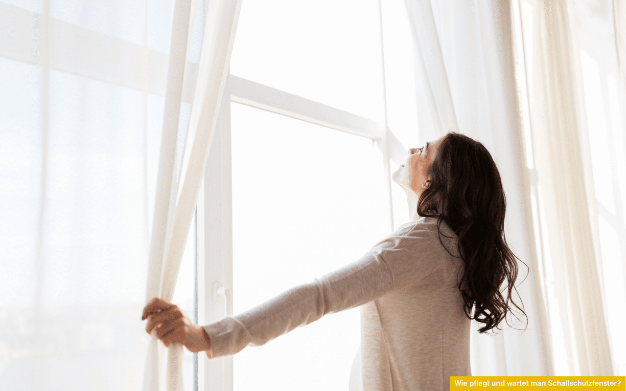 Frau öffnet weiße Vorhänge am Fenster - Wie pflegt und wartet man Schallschutzfenster zur Erhaltung von Dichtung, Funktion und Lärmschutz?
