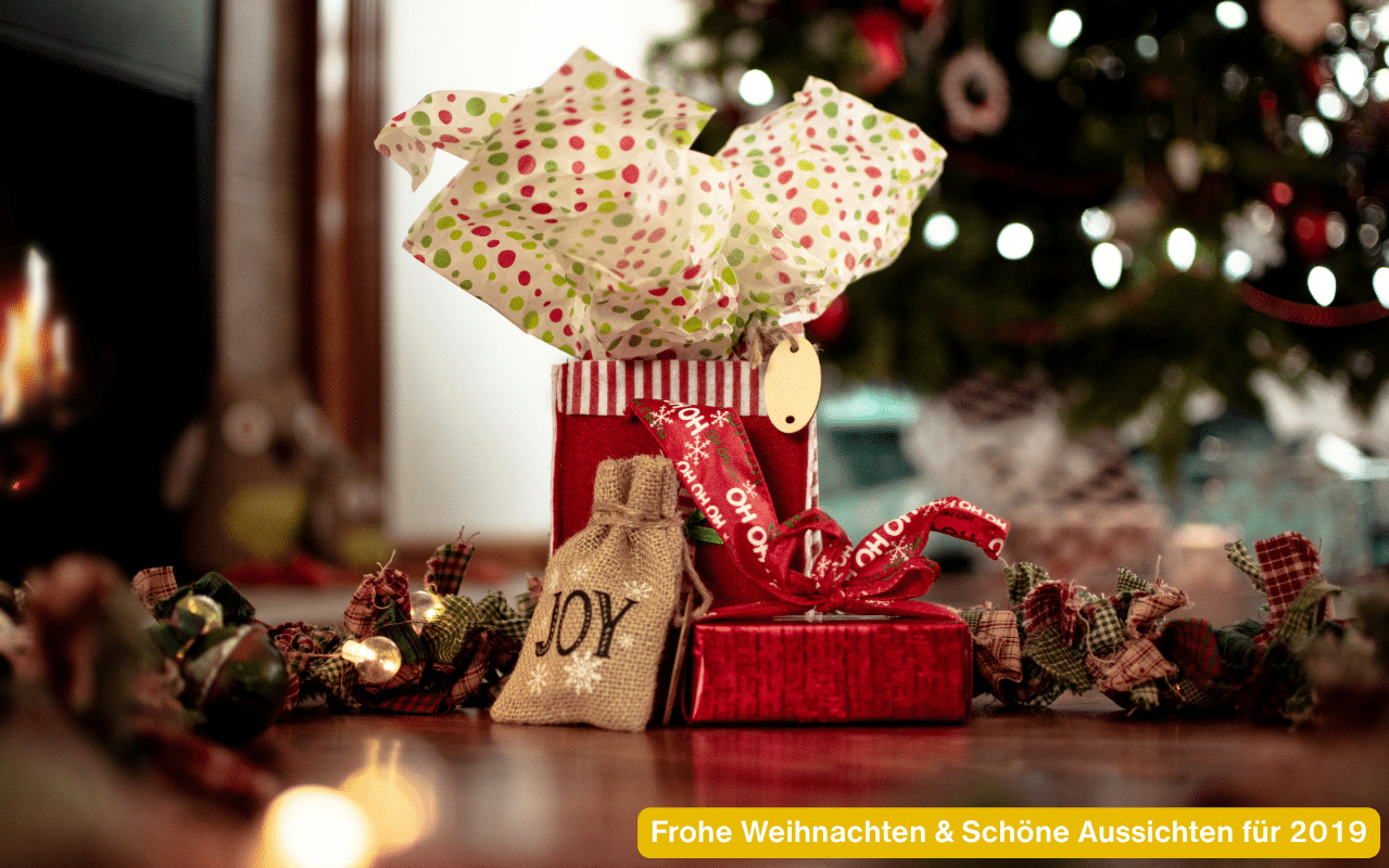 Frohe Weihnachten & Schöne Aussichten für 2019 – Geschenke und Lichter vor einem geschmückten Christbaum