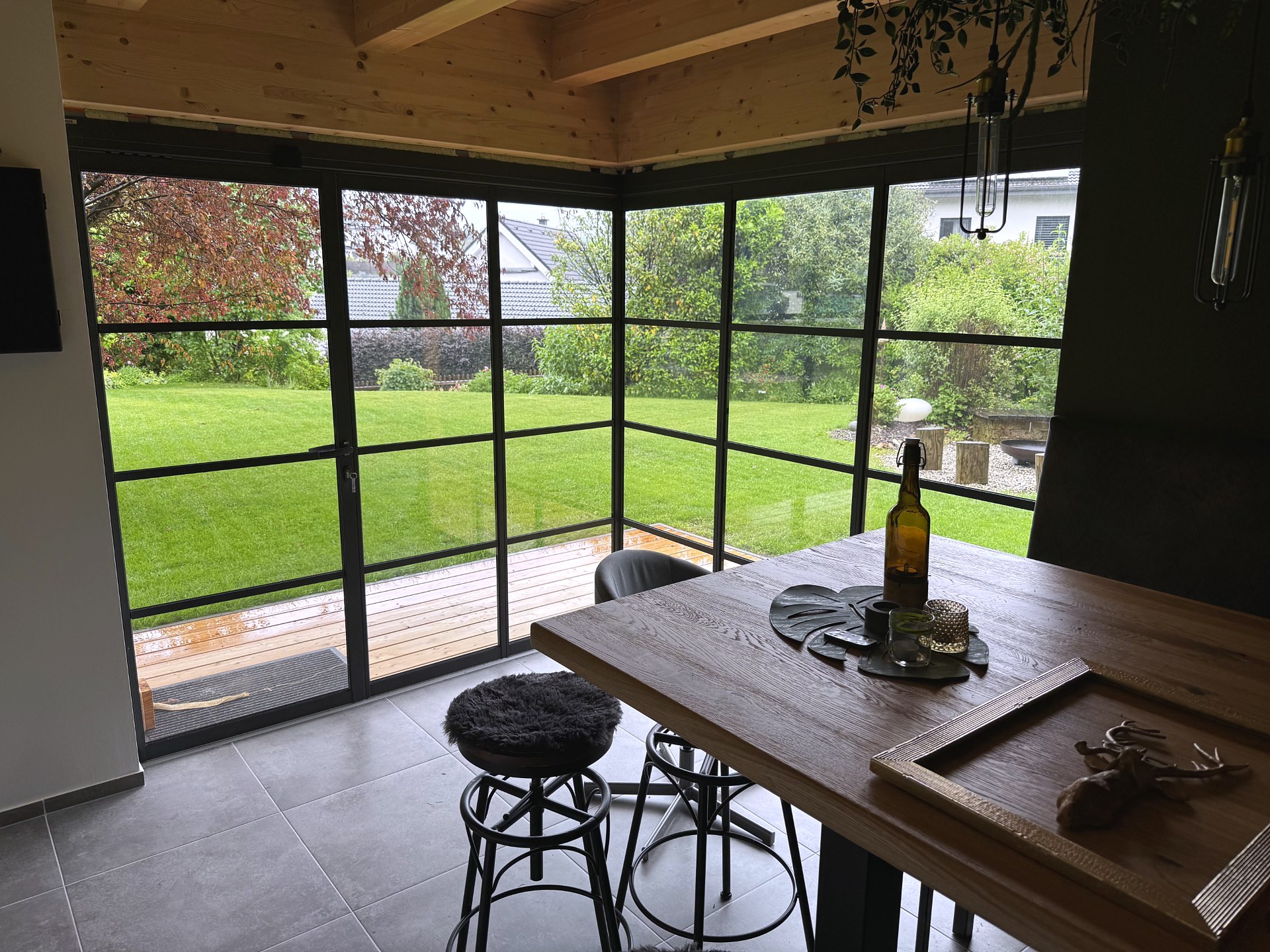 Innenansicht Gartenhaus mit Eckverglasung und Schiebe-Dreh-Elementen mit Sprossen in Dunkelgrau, Essplatz mit Holztisch, Blick in den Garten