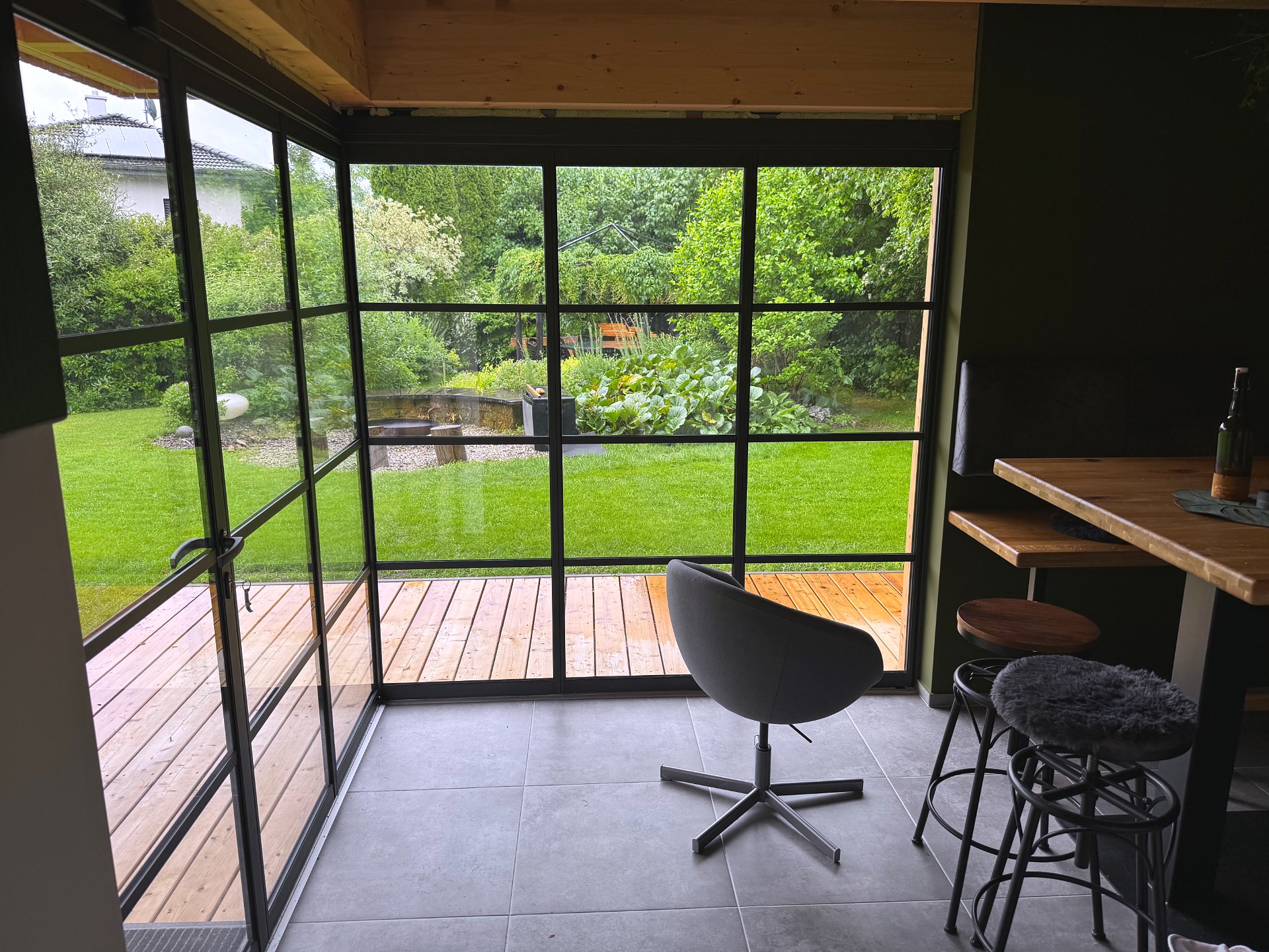 Innenansicht Gartenhaus mit geöffnetem Schiebe-Dreh-Element mit Sprossen in Dunkelgrau, Blick auf Holzterrasse und Garten