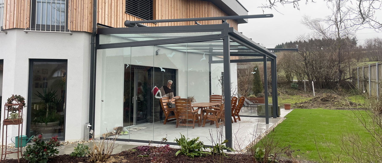 Montierte Glasschiebetüren als Windschutz für Terrassenüberdachung in Oberösterreich, bieten optimalen Schutz vor Wind.